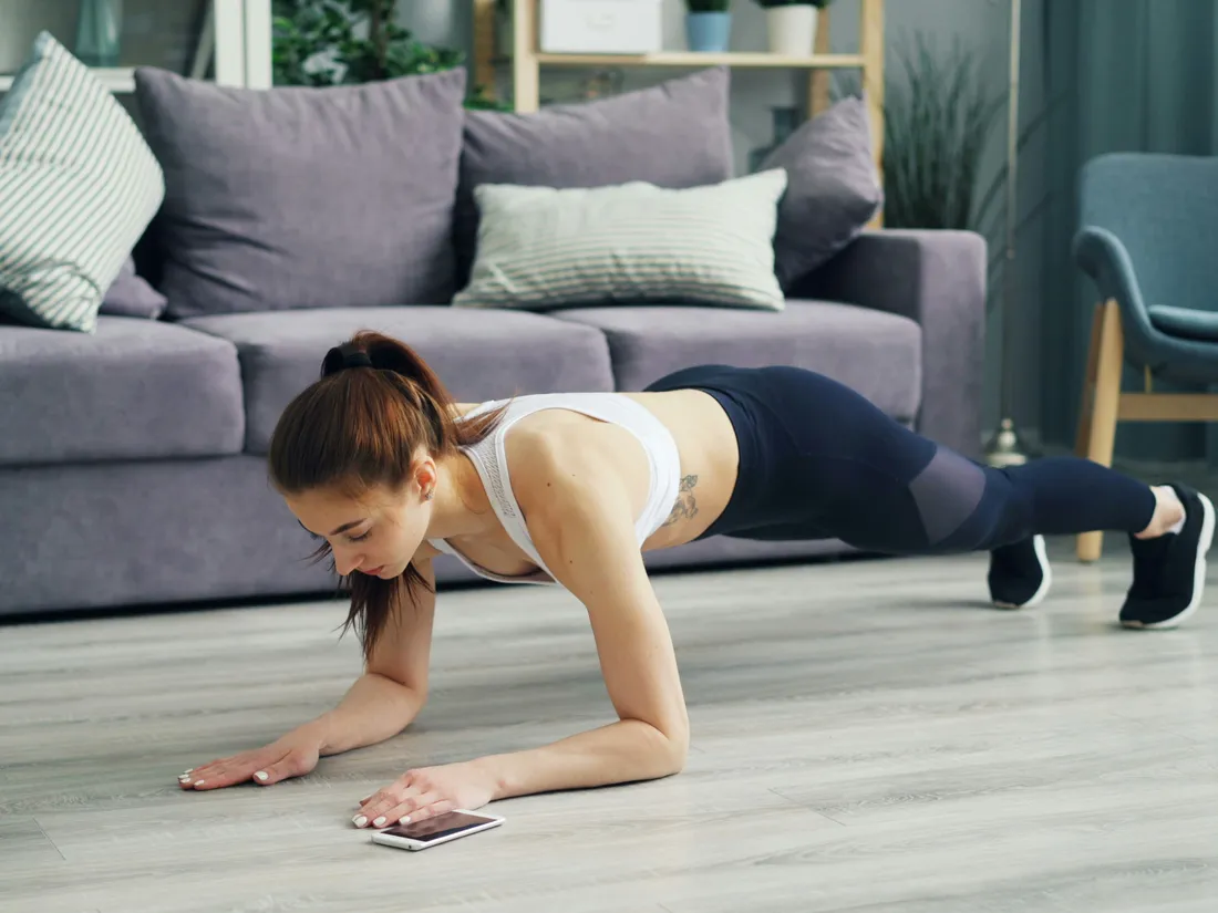 自宅で床にスマートフォンを置き、プランクをする女性